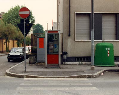 Un palo dell'illuminazione, una cabina telefonica inaccessibile, una campana per la raccolta rifiuti e un cartello stradale di divieto di accesso sono ostacoli sparsi sul marciapiede
