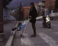 Adulto con bimbo in passeggino che attraversa la strada sulle strisce pedonali e cerca di superare il gradino del marciapiede